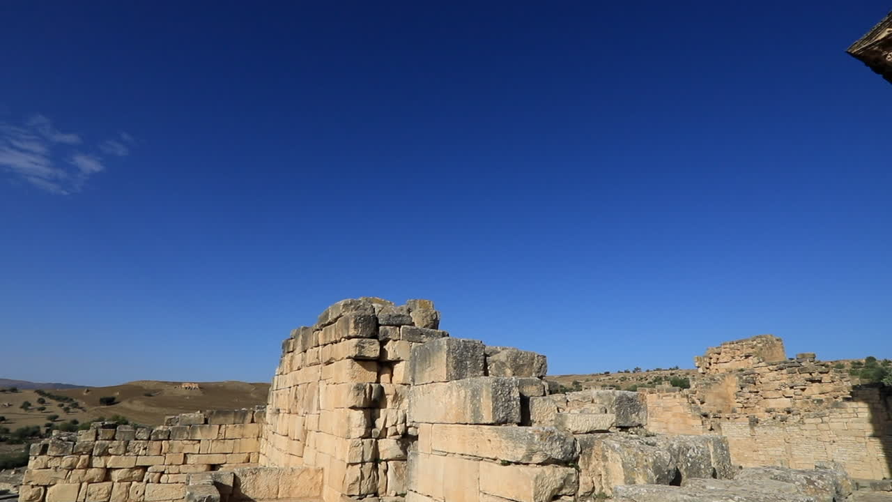 la luz de la mañana proyecta sobre las ruinas romanas de dougga contra un cielo azul claro, mostrando la arquitectura antigua