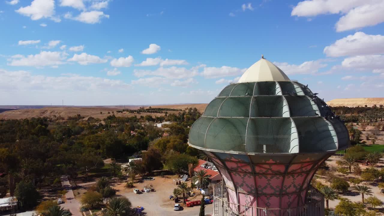 Drone circles around Neot Smadar Arts Center cooling tower under clear blue sky revealing Arava desert in the background