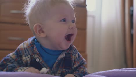 active baby in shirt plays with tube at large bed with plaid