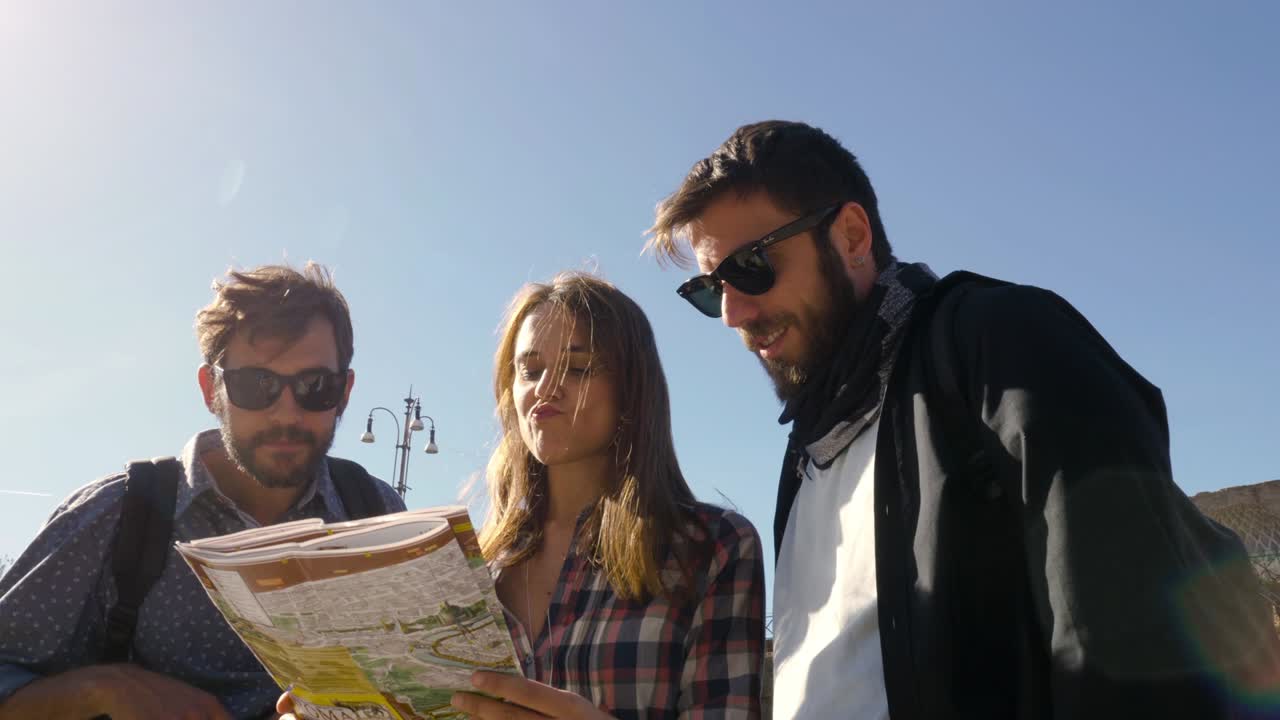 tres jóvenes amigos turistas de pie frente al coliseo en roma leyendo la guía del mapa para las direcciones apuntando con mochilas gafas de sol feliz chica hermosa de cabello largo cámara de steadycam girando alrededor de la cámara lenta