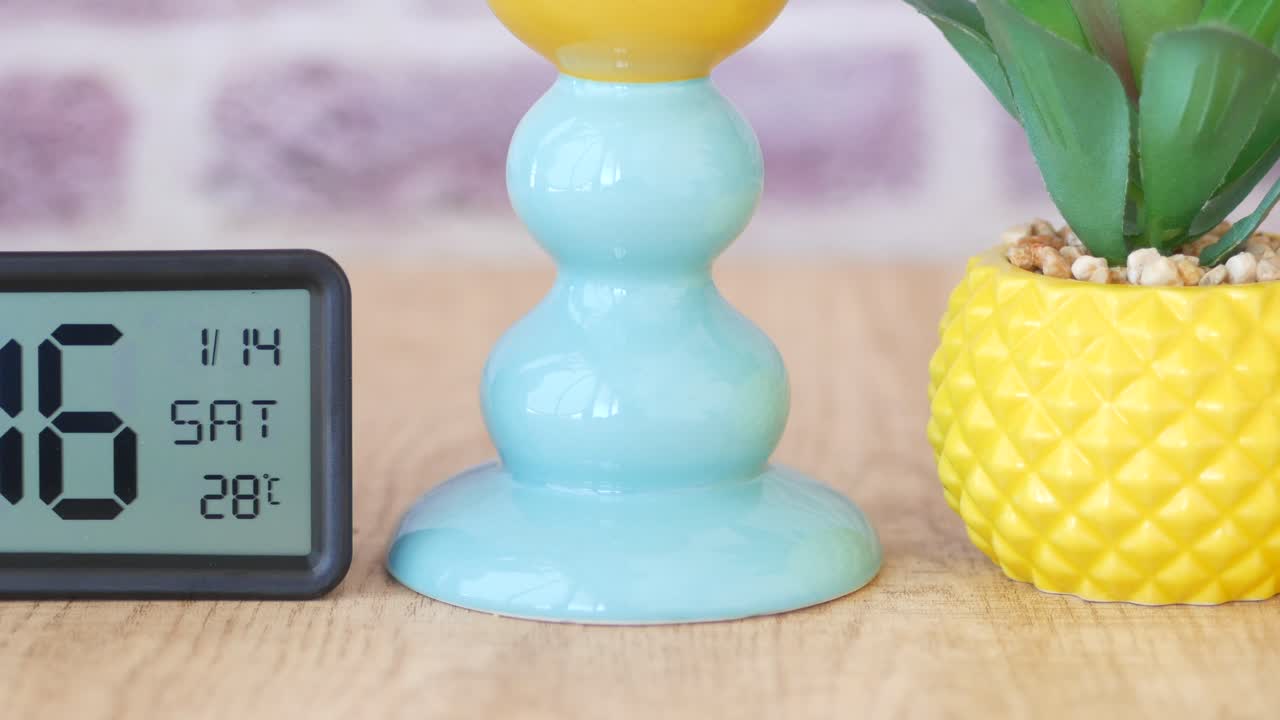 디지털 시계의 클로즈업으로 파인애플 모양의 식물 비와 배경에 세라 꽃병이 있습니다.