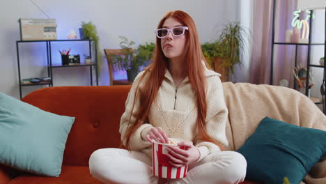 Woman-sitting-on-couch-eating-popcorn-and-watching-interesting-TV-3D-film,-sport-game-online-at-home