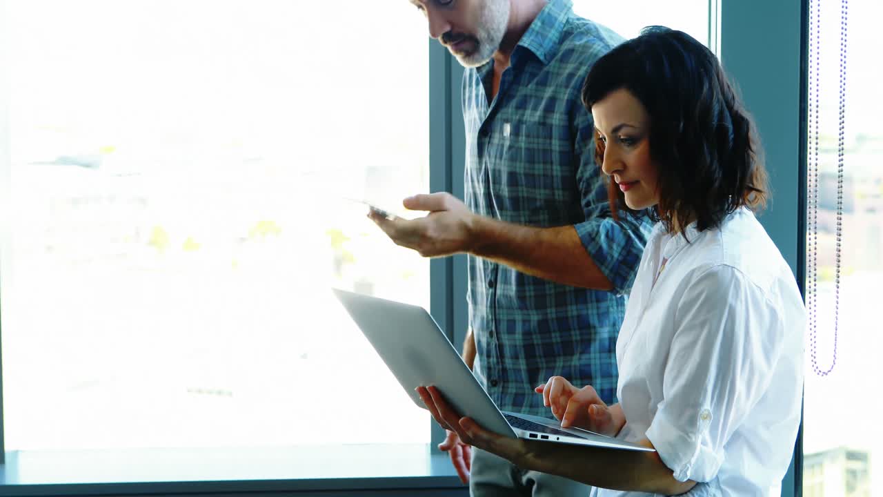 ejecutivos masculinos y femeninos usando computadora portátil cerca de la ventana