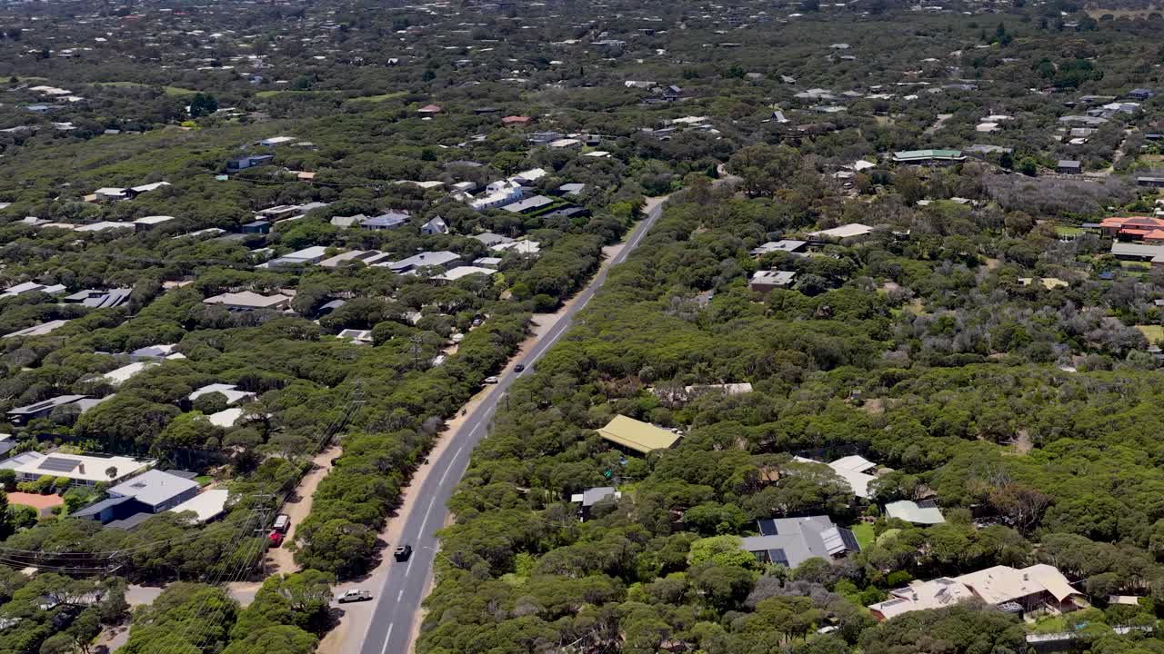 High angle drone shot tracking over residential houses and a winding road in lush greenery