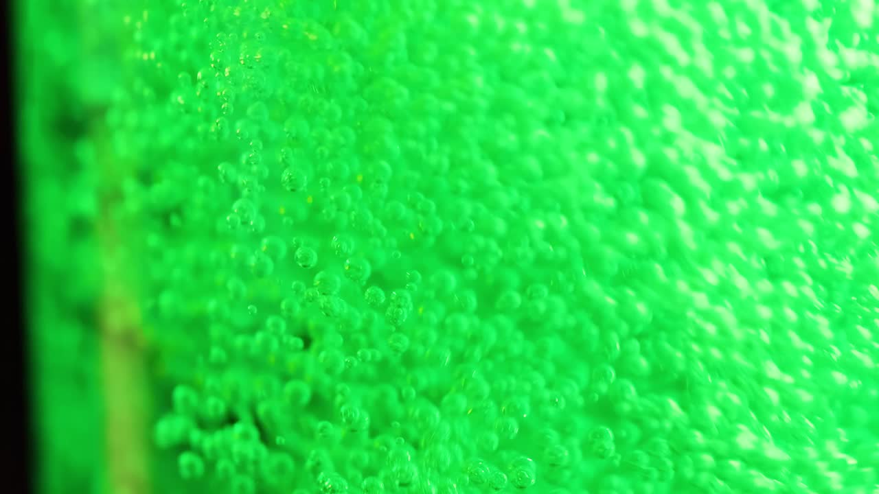 Close-up view of green bubbles ascending in a vibrant liquid, showcasing dynamic movement and effervescence.