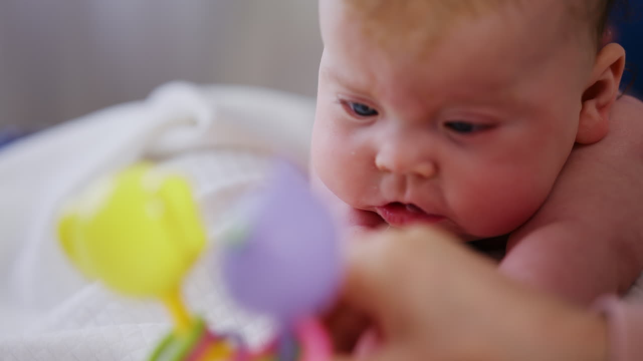 Woman trying to distract a crying baby lying on a blanket during massage with a toy