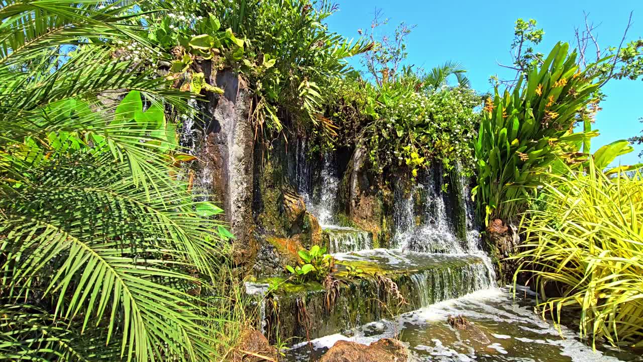 Air Terjun Buatan Dikelilingi Vegetasi Hijau dan Bunga-bunga