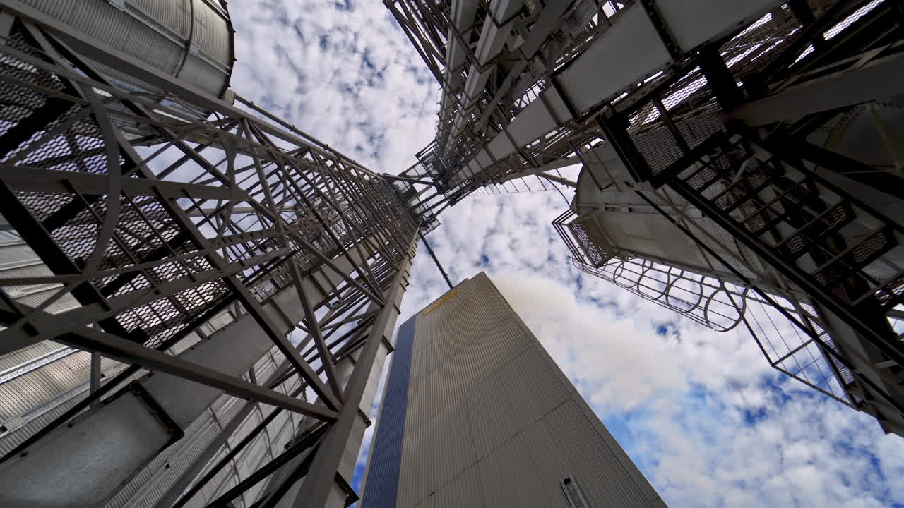 Industry. High metal stairs on the industrial plant. Modern territory for grain storage. Steel frame on warehouse outdoors. View from below.