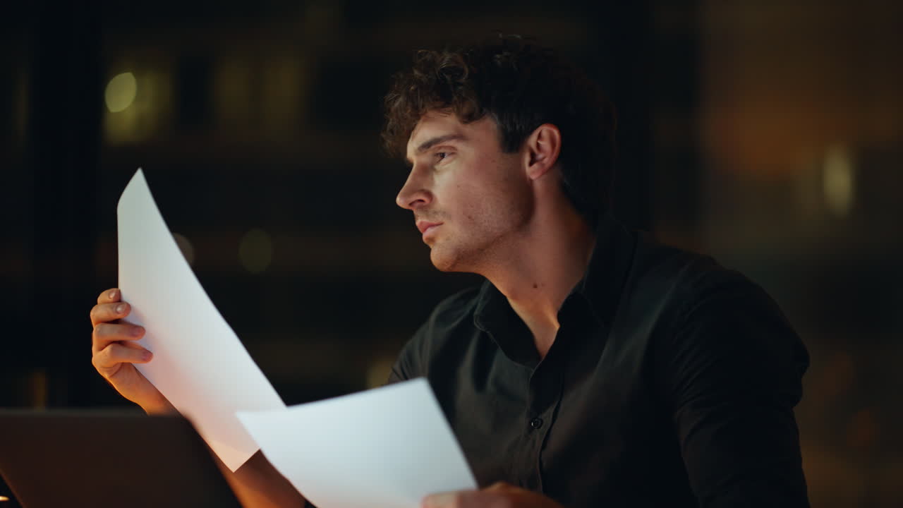 Tensed freelancer reading documents at dark workplace closeup. Worried man