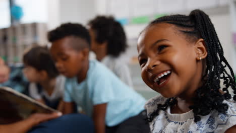 Porträt-Einer-Grundschülerin-Mit-Lehrerin,-Die-Im-Hintergrund-Der-Klasse-Vorliest