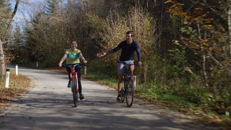 couple cycling on a forest trail, holding hands and having fun, front view