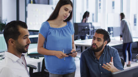 Caucasian-businesswoman-standing-in-discussion-with-two-mixed-race-male-colleagues-at-their-desk