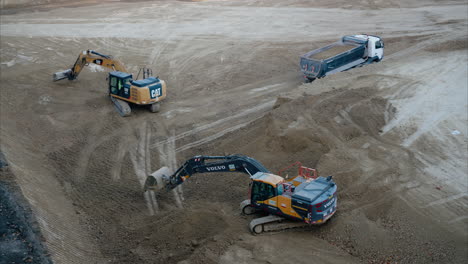 excavators digging dirt on an active construction site while dump truck hauls loaded dirt. heavy machinery work in unison to prepare the site for foundation laying, and further construction activities