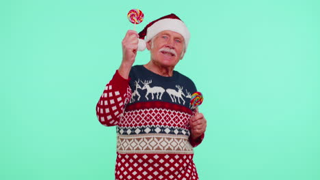 Senior-grandfather-in-Christmas-sweater-holding-candy-striped-lollipops,-dancing-making-silly-faces