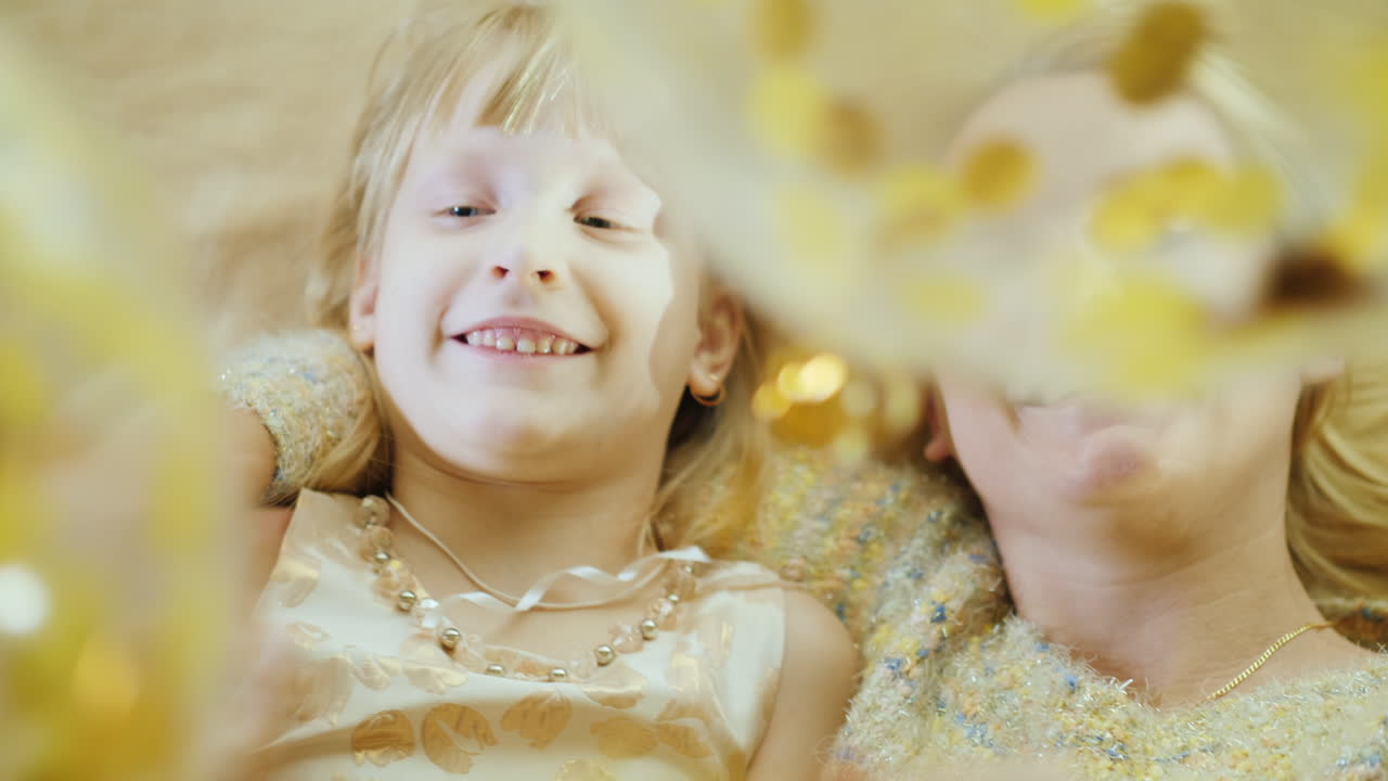 한 소녀와 그녀의 어머니가 웃으며 풍선을 가지고 놀고 있습니다. 그들은 침대 머리에 나란히 누워 있습니다.