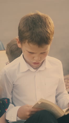 schoolchildren in classic dressing prepare for difficult exam reading textbooks sitting on road in sunny morning closeup