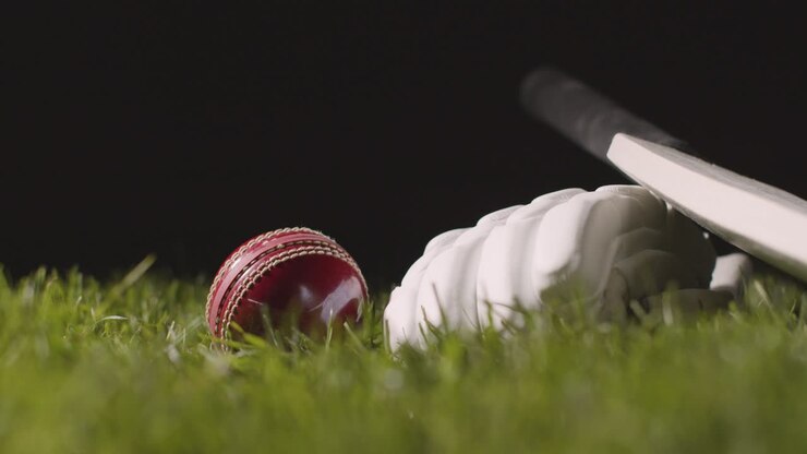 Natura morta di cricket con primo piano di mazza, palla e guanti adagiati sull'erba 1