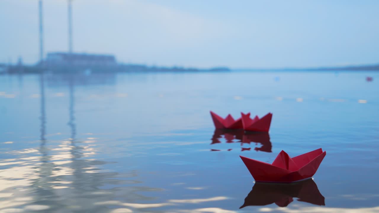 Childish paper boats floating on the water surface on the blurred background. Three red homemade ships on the river