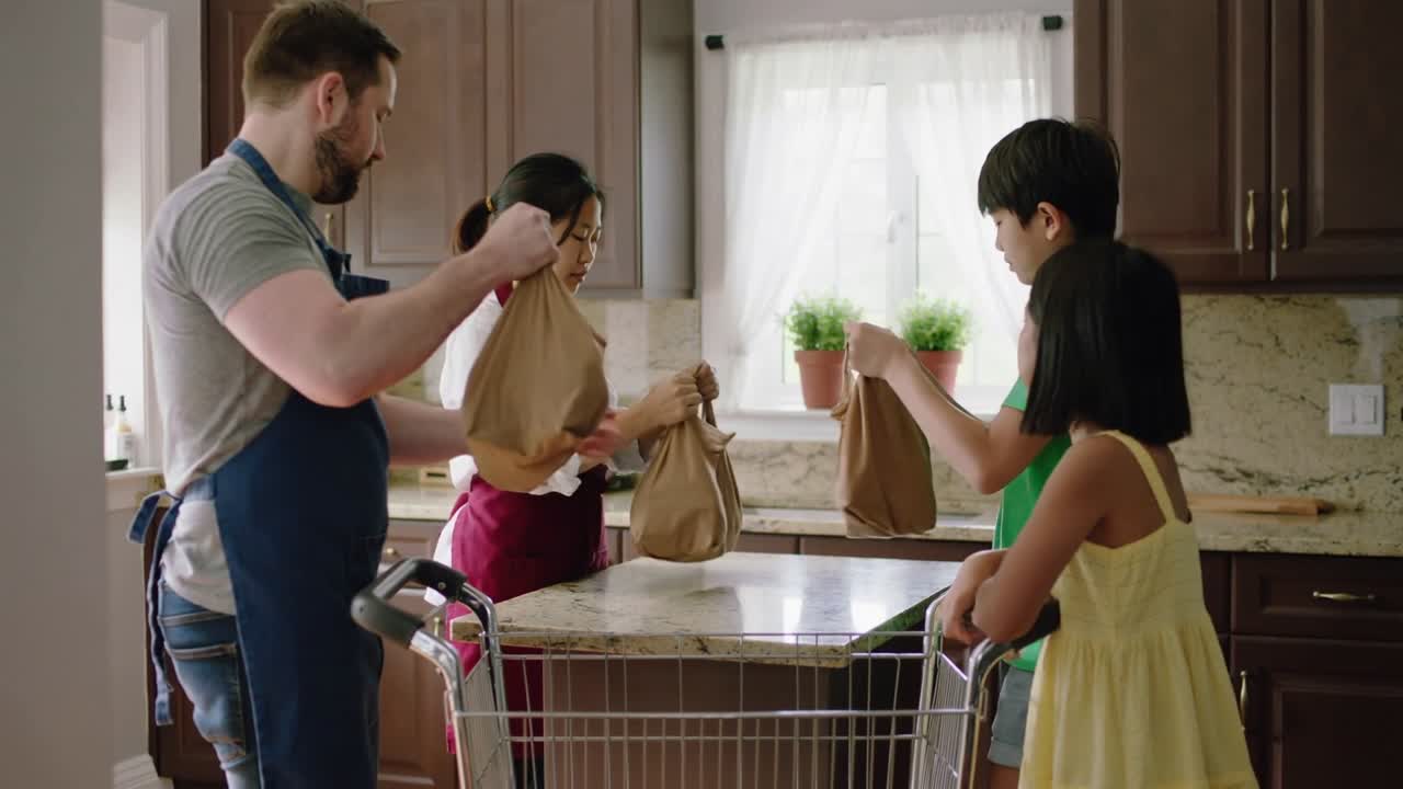 Upon cart arrival family in aprons lifting handing arranging paper bags at kitchen island to unpack
