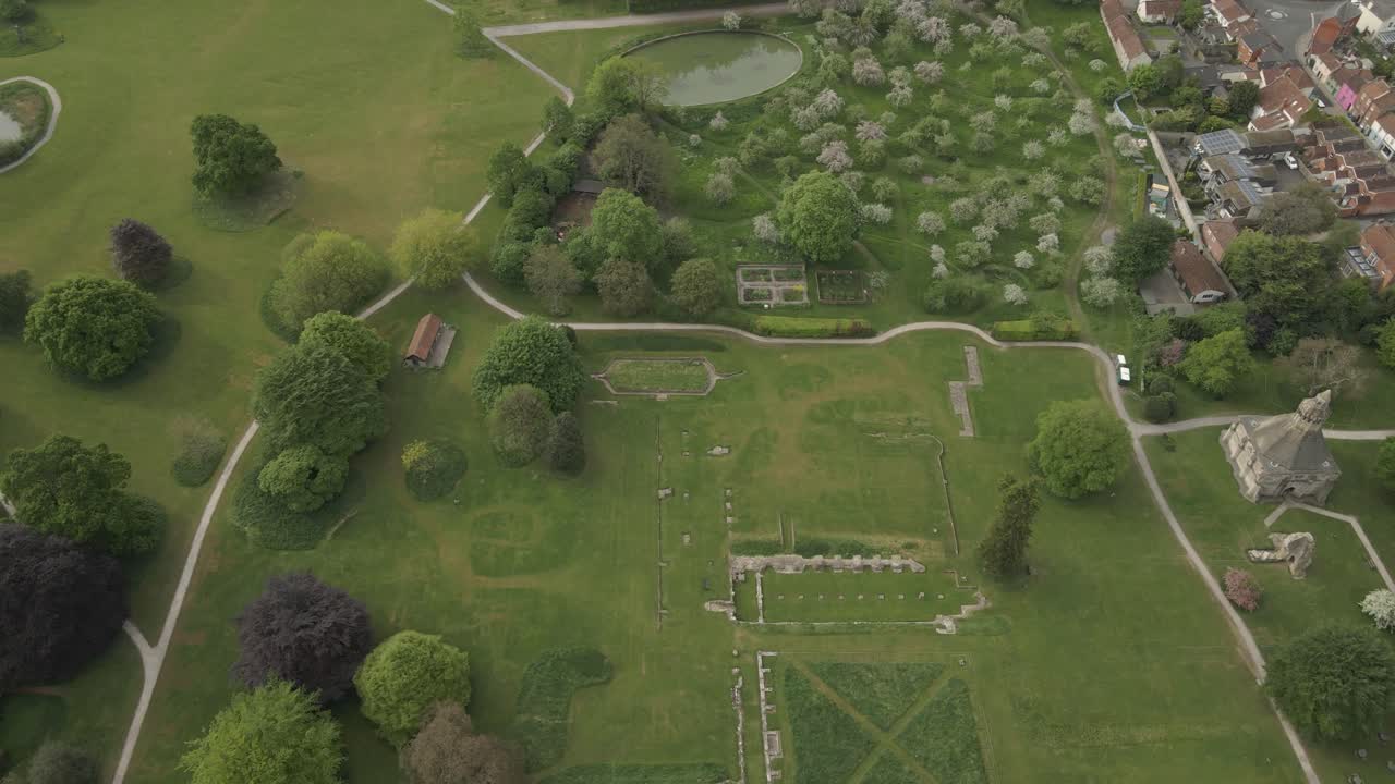 Aerial view of Glastonbury abbey ruins, drone moving forward and camera facing down over the abbey gardens and ruins,. 4K, 60fps.