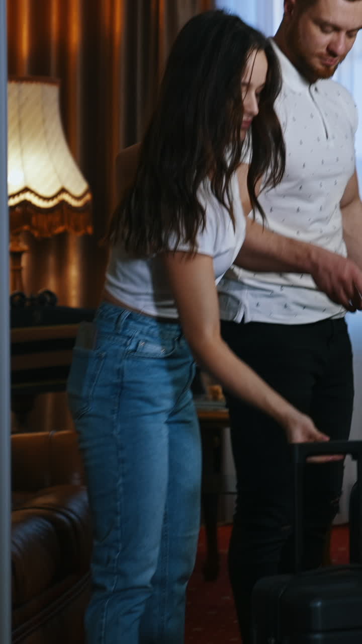 Young couple with baggage. Beautiful woman and handsome man holding their suitcases before leaving the hotel room. Family vacation. Vertical video