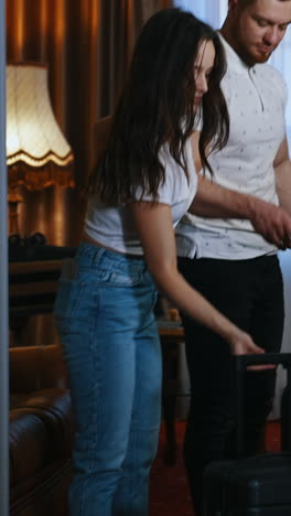 young couple with baggage. beautiful woman and handsome man holding their suitcases before leaving the hotel room. family vacation. vertical video