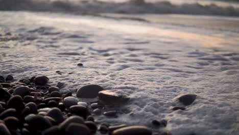 Nahaufnahme-Von-Strandwellen-Und-Schaum,-Der-Durch-Kieselsteine-Und-Felsen-In-Zeitlupe-Sprudelt