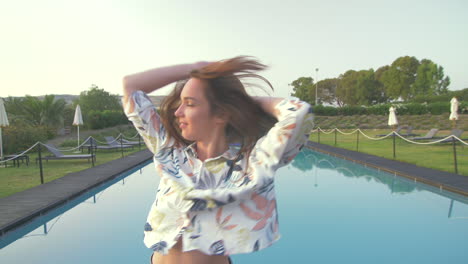 mujer con una camisa blanca y pantalones cortos baila cerca de una piscina en un día soleado