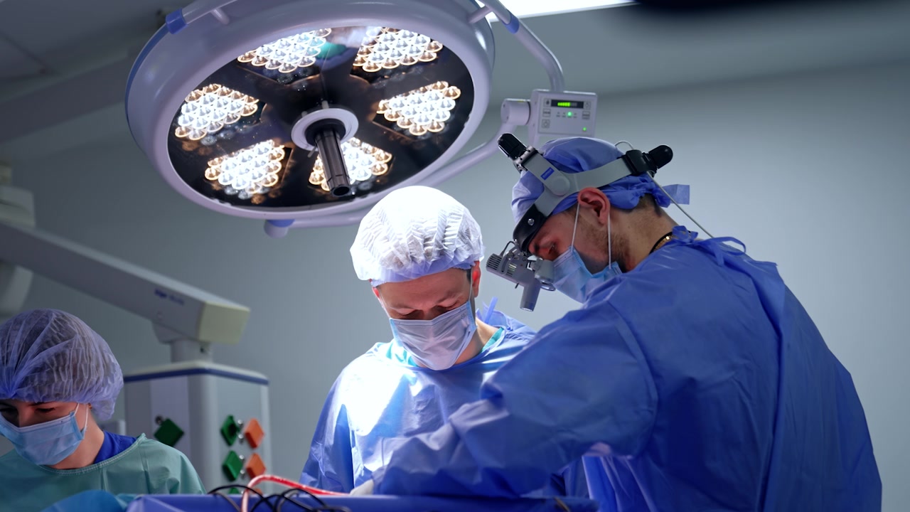 Due chirurghi caucasici maschi collaborano durante un'operazione. Un'infermiera assiste alla neurochirurgia