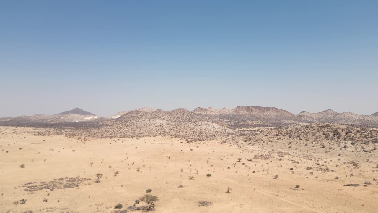 Dronekuvaa syrjäisestä aavikkomaisemasta vuorineen Namibiassa, esitellen laajaa kuivaa maastoa ja dramaattista luonnonmaisemaa.