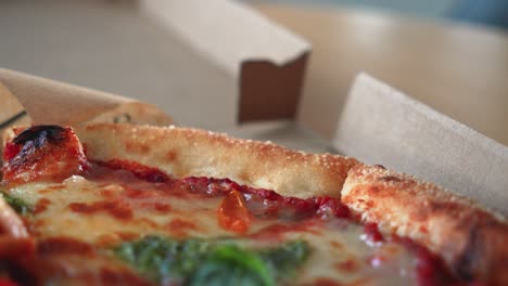 closeup shot of tasty italian pizza with pesto sauce in a cardboard pizza box on the table, zoom out