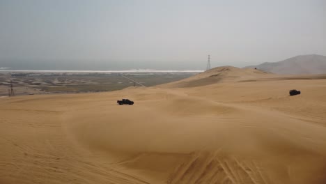 Vista-Aérea-Alrededor-De-Camiones-Que-Conducen-Sobre-Dunas-En-Nublado-Ica,-Lima,-Perú---Dando-Vueltas,-Disparo-De-Drones