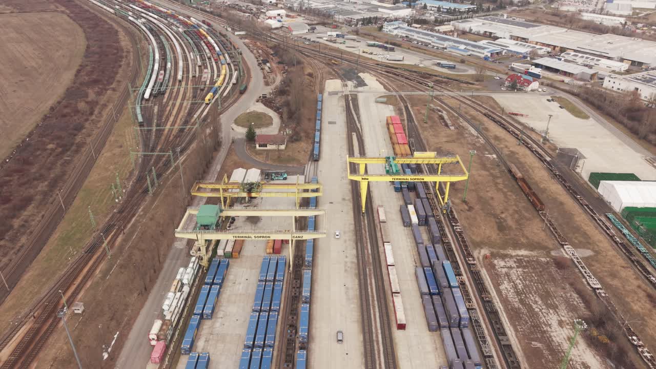 Drohnenansicht eines großen intermodalen Frachtterminals mit Frachtcontainern und Eisenbahngleisen. Gelbe Portalkräne arbeiten über langen Güterzügen.