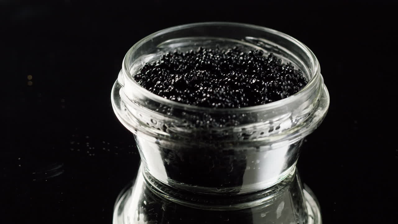 Caviale nero in un barattolo di vetro su sfondo nero riflettente