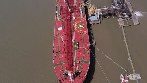 red industrial ship at loading dock harbour on water, aerial flyover