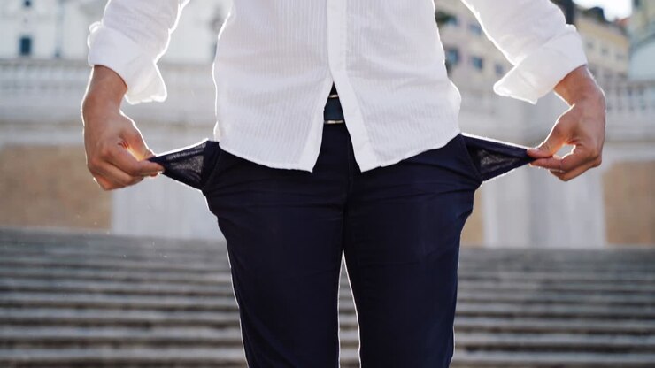 Uomo triste seduto sulle scale all'aperto che si tocca le tasche dei pantaloni. Giovane turista deluso che mostra le sue tasche vuote per strada. Nessun denaro nelle tasche. Primo piano di qualcuno che cerca denaro. Scoprire il mondo è costoso.