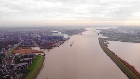 Alta-Vista-Aérea-Sobre-El-Río-Noord-En-Un-Día-Nublado-Con-La-Tienda-De-Carga-Strelitzia-Pasando-Crezeepolder-En-Alblasserdam