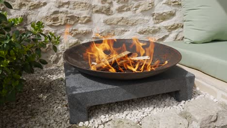 Outdoor-fire-burns-in-round-cast-iron-fire-pit-in-a-bright-sunny-day