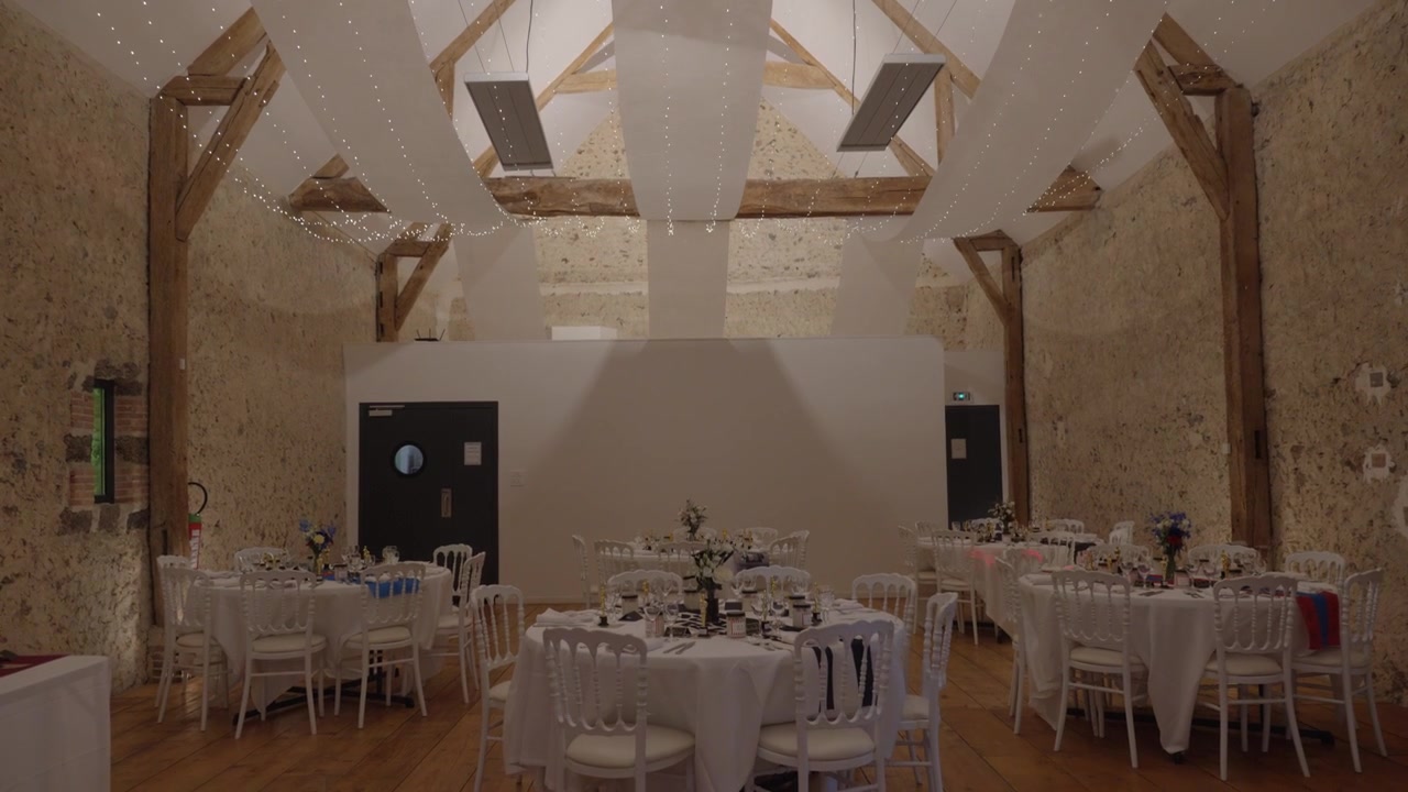 White fabric drapes and string lights decorate wooden ceiling beams at a wedding reception, tilt downward