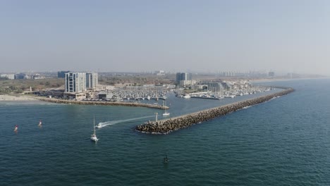 several ships and kite surfers sail across the clear mediterranean as they leave the marina of herzeliya in israel on a sunny day