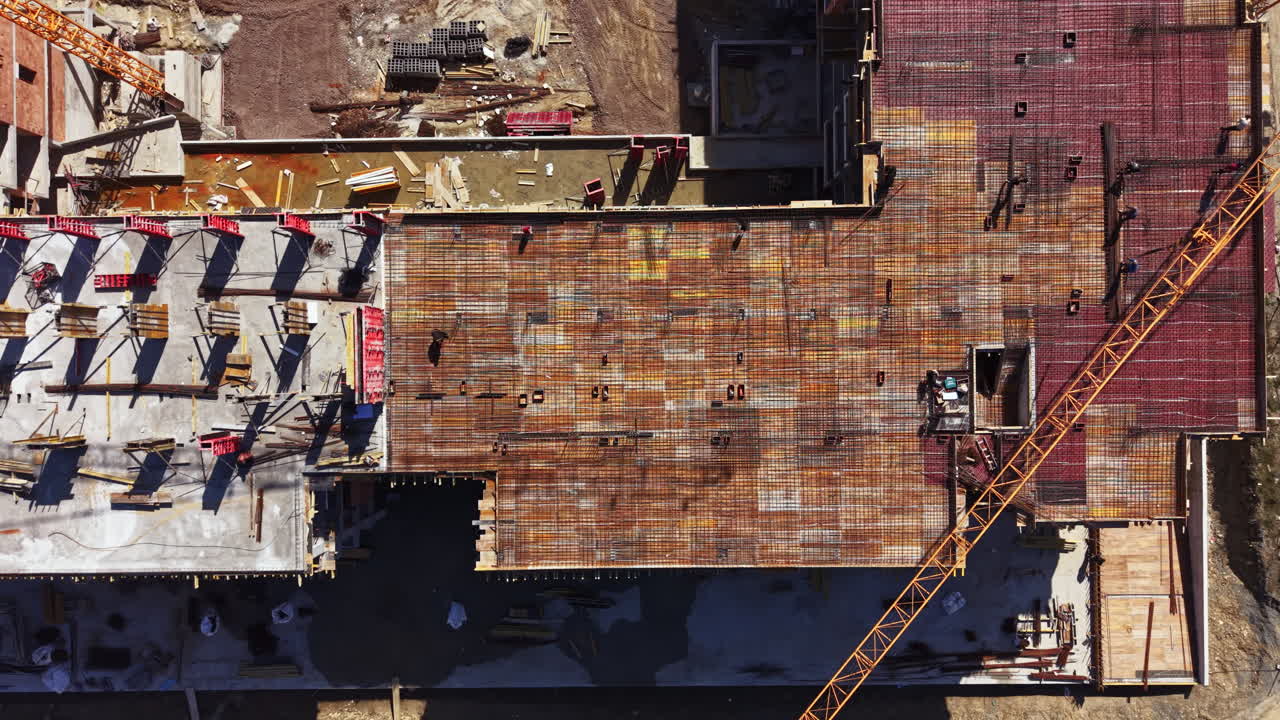 Construction site shows building progress with a flat roof and crane at work in the background on a clear day near a busy area