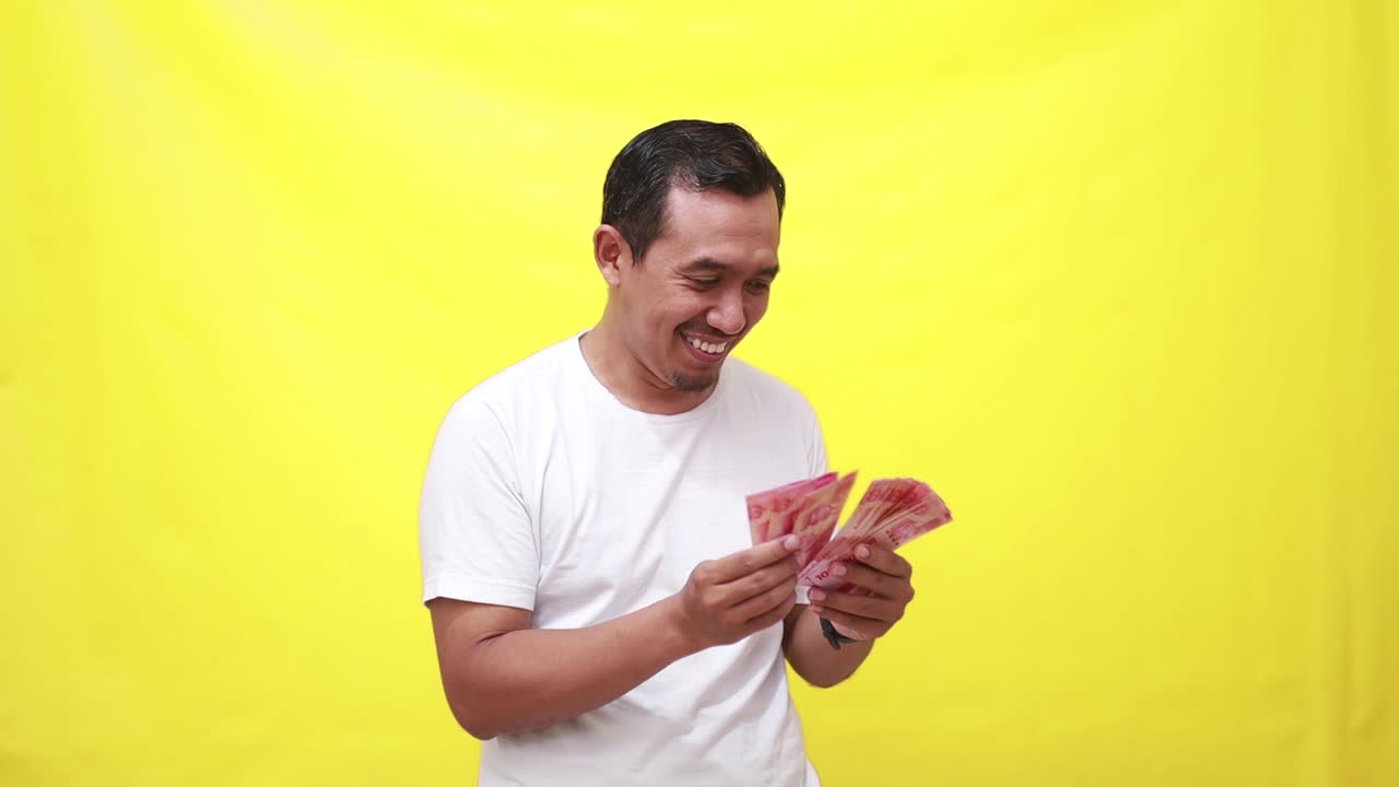Excited surprised asian adult man holding and counting Indonesian banknotes money