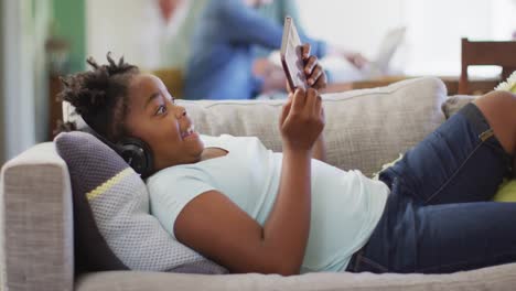 Glückliches-Afroamerikanisches-Mädchen,-Das-Auf-Dem-Sofa-Liegt-Und-Ein-Tablet-Benutzt
