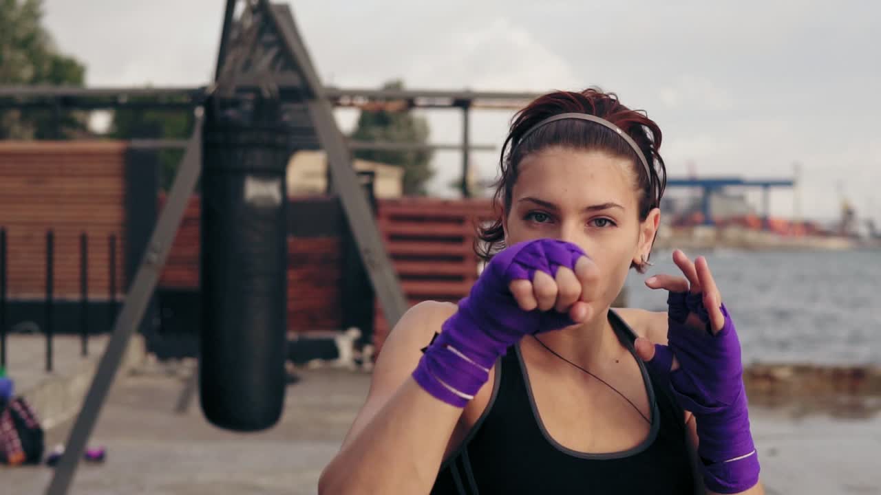 vista de cerca de una joven entrenando con las manos envueltas en cintas de boxeo púrpura y mirando a la cámara.