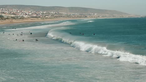 wide view of a beach, shore and people surfing on sea waves in agadir, morocco