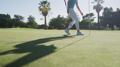 Caucasian-female-golf-player-reaching-for-a-ball-standing-on-golf-field