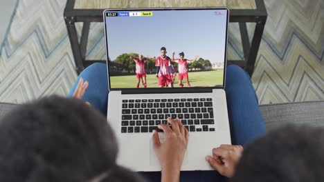 video de dos personas afroamericanas sentadas en el sofá y viendo un partido de fútbol en una computadora portátil