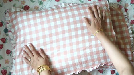 a woman's hands rest on a pink checkered pillow on a bed with strawberry print sheets