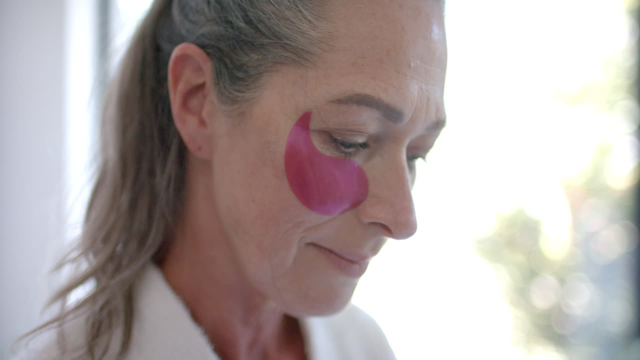 Applying under-eye patches, mature woman focusing on skincare routine at home