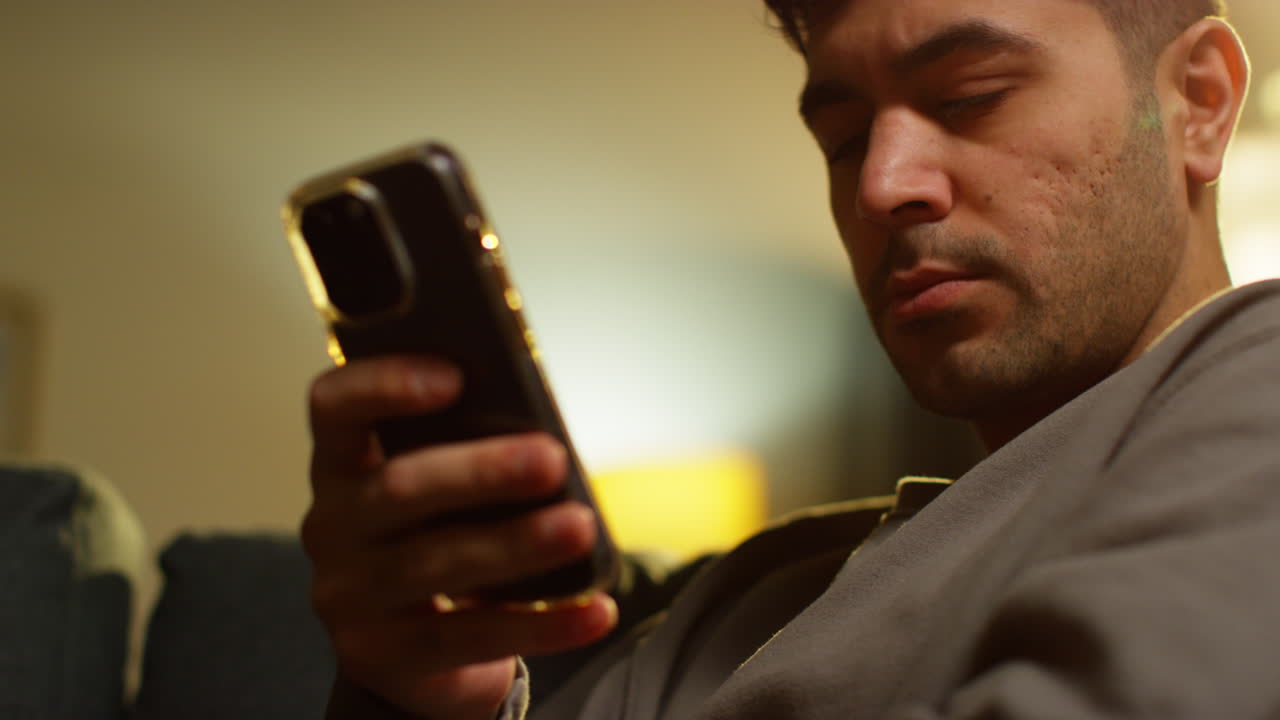 집에서 저녁을 보내고 소파에 앉아 휴대전화를 들고 인터넷이나 소셜 미디어 스트리밍 콘텐츠를 스크롤하는 젊은 남자의 클로즈업